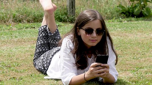 躺在草地上的女孩正在使用智能手机视频的预览图
