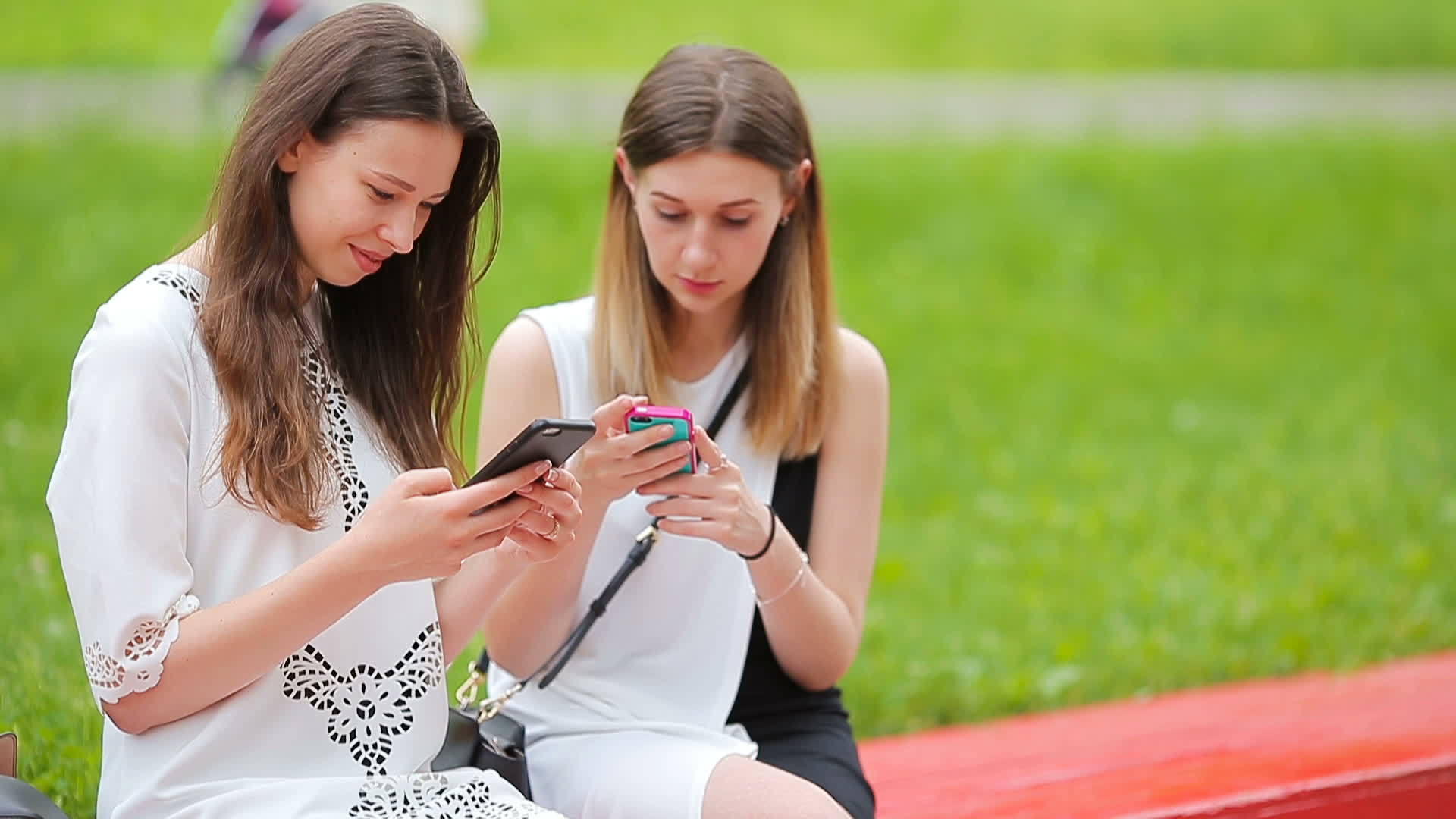 两个女孩在户外使用智能手机两个女人坐在公园里喝咖啡视频的预览图