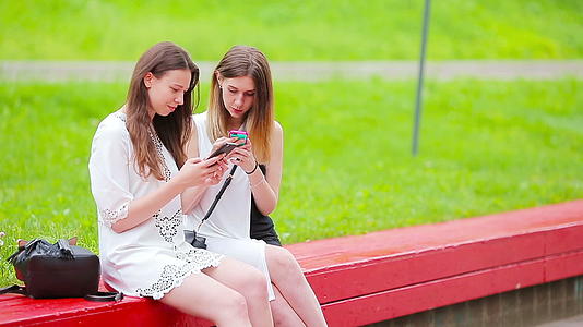 两个女孩在户外使用智能手机两名妇女坐在公园里使用智能手机视频的预览图