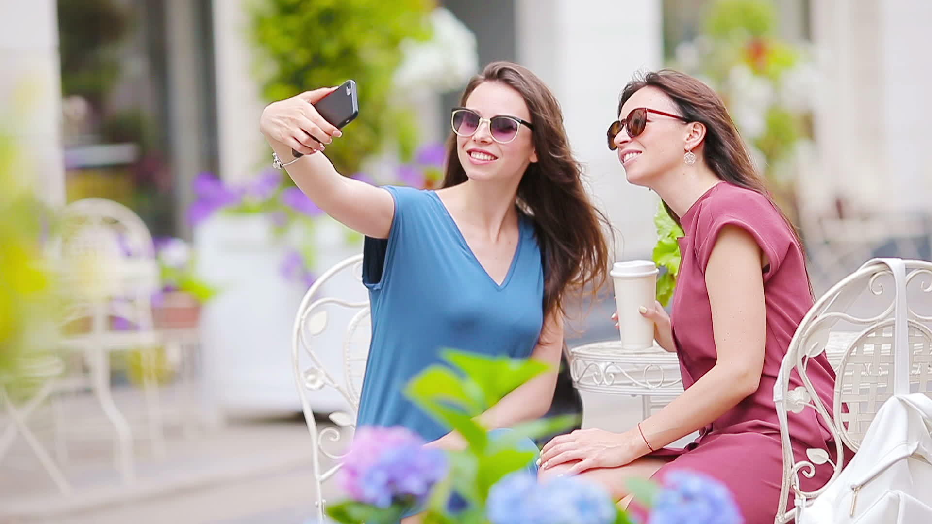 两个年轻女孩在户外咖啡馆用智能手机自拍两名女性购物视频的预览图