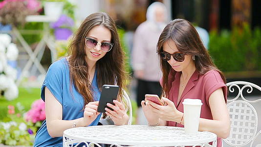 两个年轻女孩在户外咖啡馆使用智能手机两个女人购物后购物视频的预览图