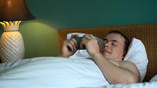 躺在床上的男人正在用智能手机申请笑声视频的预览图