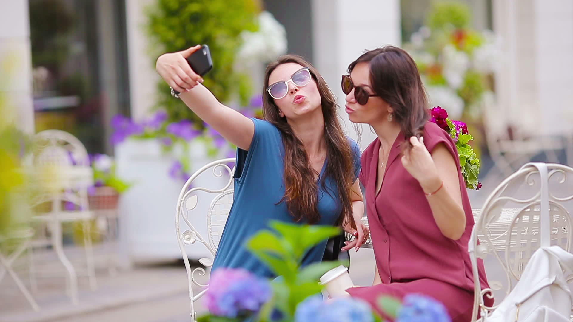 两个年轻女孩在户外咖啡馆用智能手机自拍视频的预览图