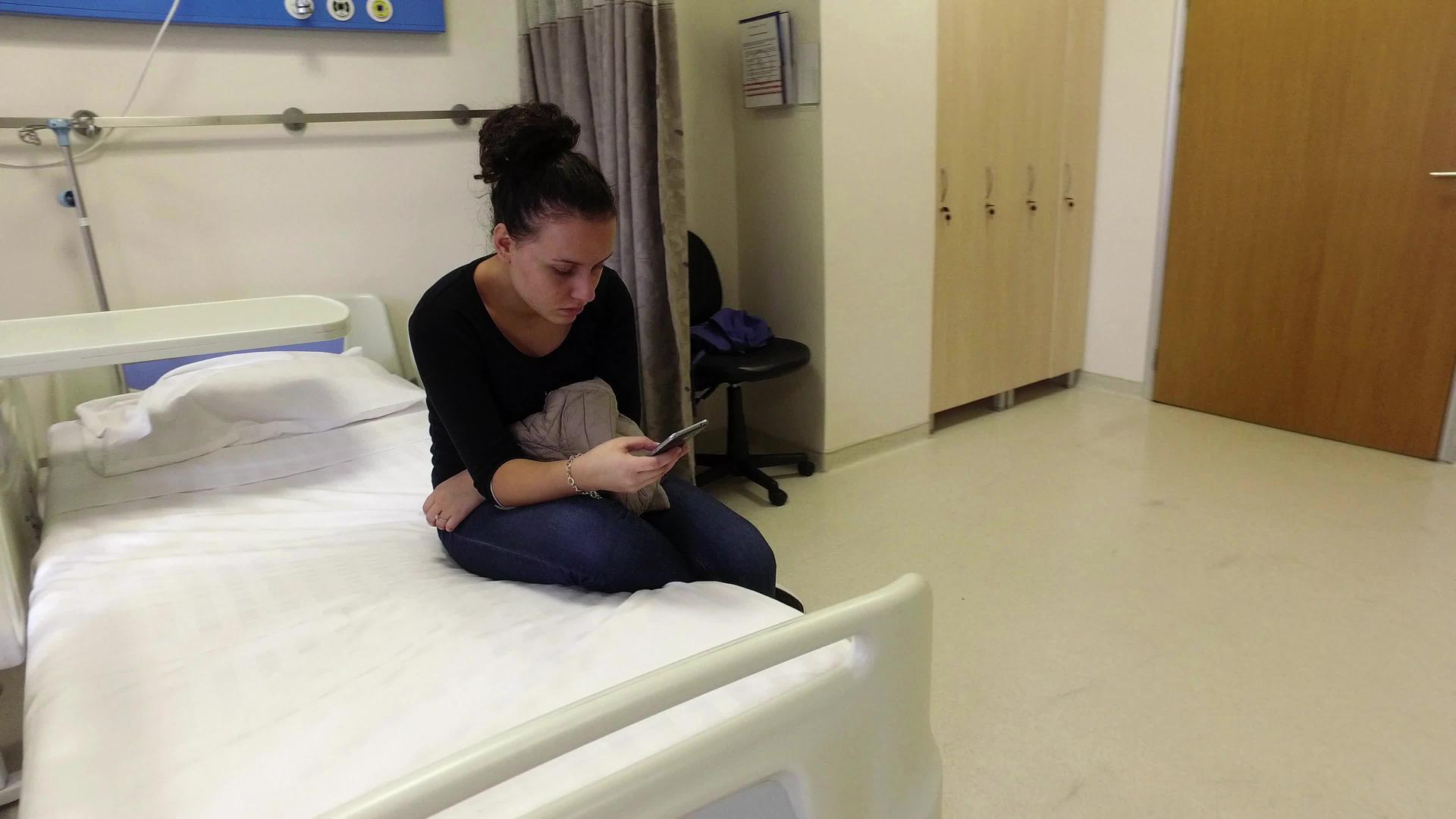 吸引人的女孩在医院发短信坐在床上在手机上输入视频的预览图