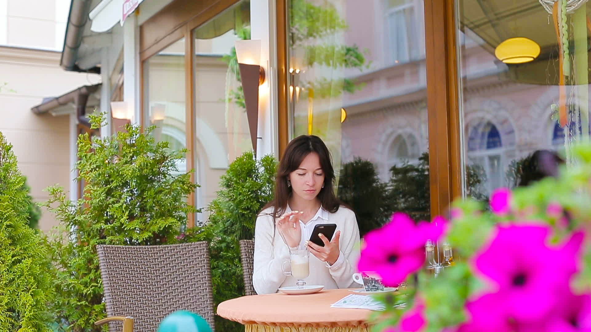 喝一杯咖啡的年轻女孩用智能手机在户外咖啡馆拍照和散步视频的预览图