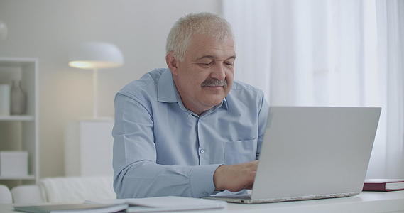 有胡子的中年男子在笔记本电脑键盘上打字浏览互联网网站视频的预览图