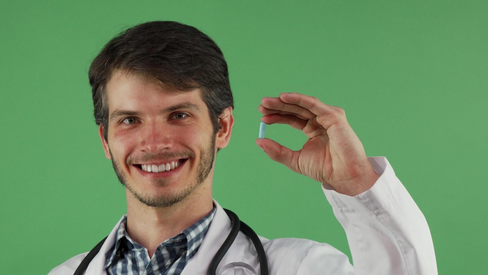 快乐的男医生在绿色背景下用蓝色药片微笑视频的预览图