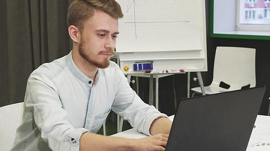 有吸引力的年轻男子在办公室使用智能手机和笔记本电脑视频的预览图