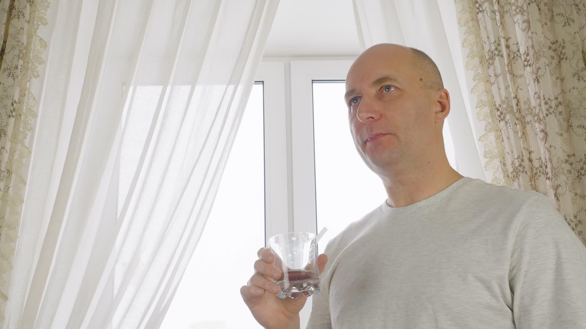 家庭厨房窗户背景玻璃中的成年秃头成年男子饮用水视频的预览图