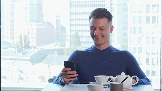 快乐的英俊男人笑得很开心用他的智能电话喝茶视频的预览图