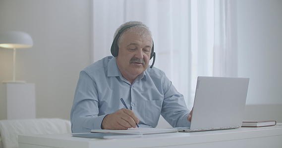 老人在家工作用笔记本和同事、伙伴在纸上交流视频的预览图