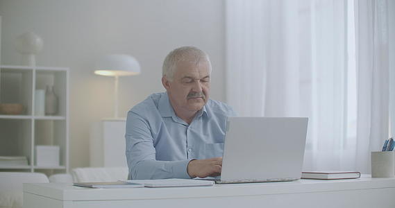 疲惫的头痛中年男子在家工作笔记本电脑头痛过度伸展视频的预览图