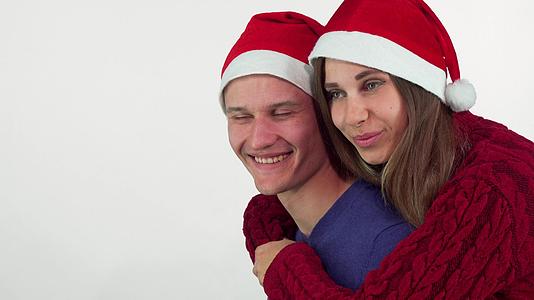 快乐的年轻夫妇戴着圣诞帽拥抱笑着看着远处视频的预览图