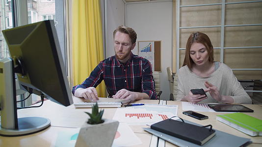 男人在电脑上工作女人看智能手机笑视频的预览图