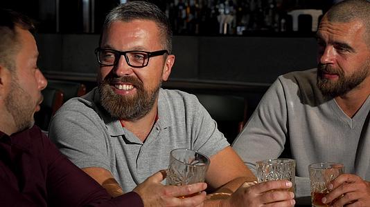 一群成熟的男性朋友在酒吧里大笑谈论威士忌酒杯视频的预览图
