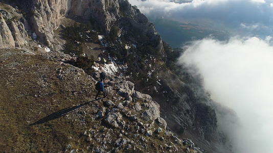 那个带着背包的徒步旅行者正站在云层上方山顶的陡峭边缘视频的预览图