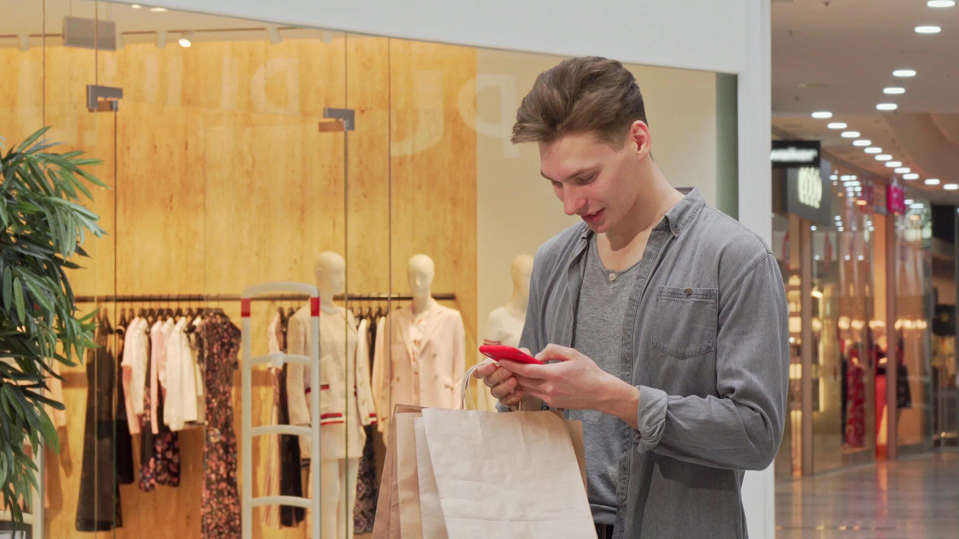 购物中心购物时年轻人微笑着使用智能手机视频的预览图