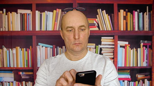白人成人天主教徒使用智能手机bookshelf背景视频的预览图