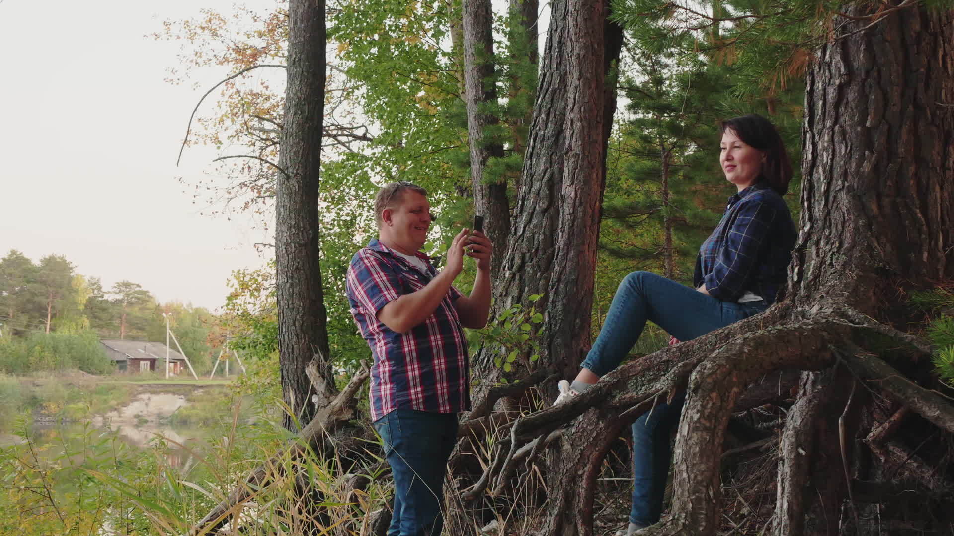 男人用手机在针叶林里给女人拍照快乐的女人在松树林里视频的预览图