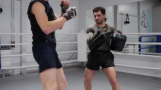 在与教练的个人训练中男拳击手用腿踢拳击垫战斗机视频的预览图