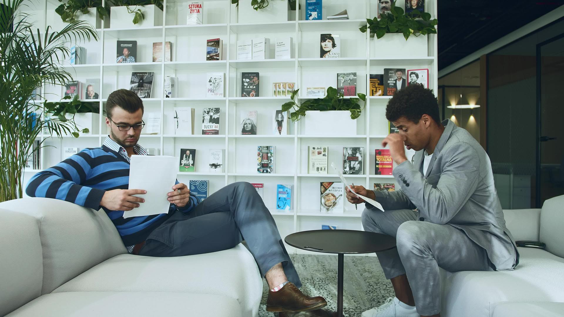 坐在现代办公室的成年多种族男子在沙发上寻找纸质文件视频的预览图