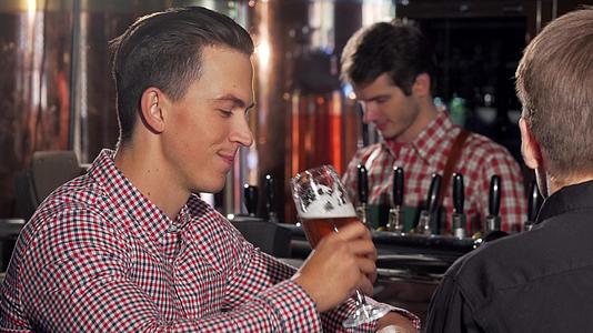 英俊快乐的男人在酒吧里享受美味的啤酒和朋友聊天视频的预览图