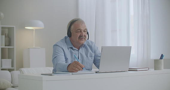 中年男子通过互联网使用笔记本电脑和耳机在复印本中录取视频的预览图