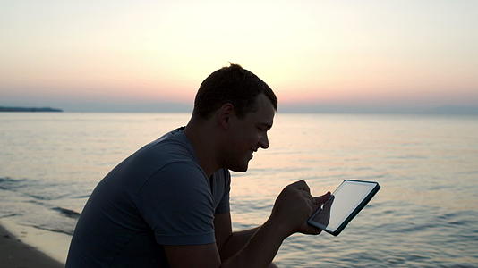 在海滩上使用平板电脑的人视频的预览图