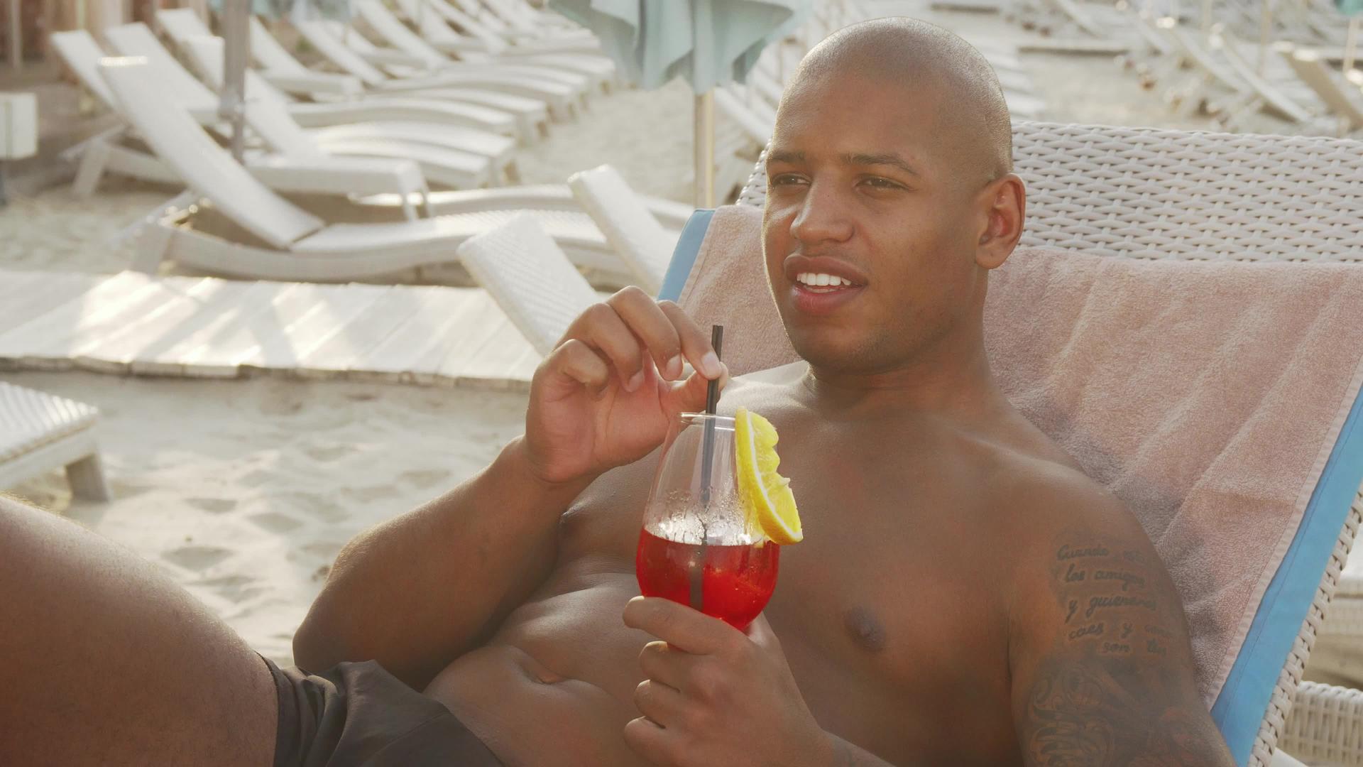 英俊的非洲男人在海滩上放松时喝鸡尾酒视频的预览图