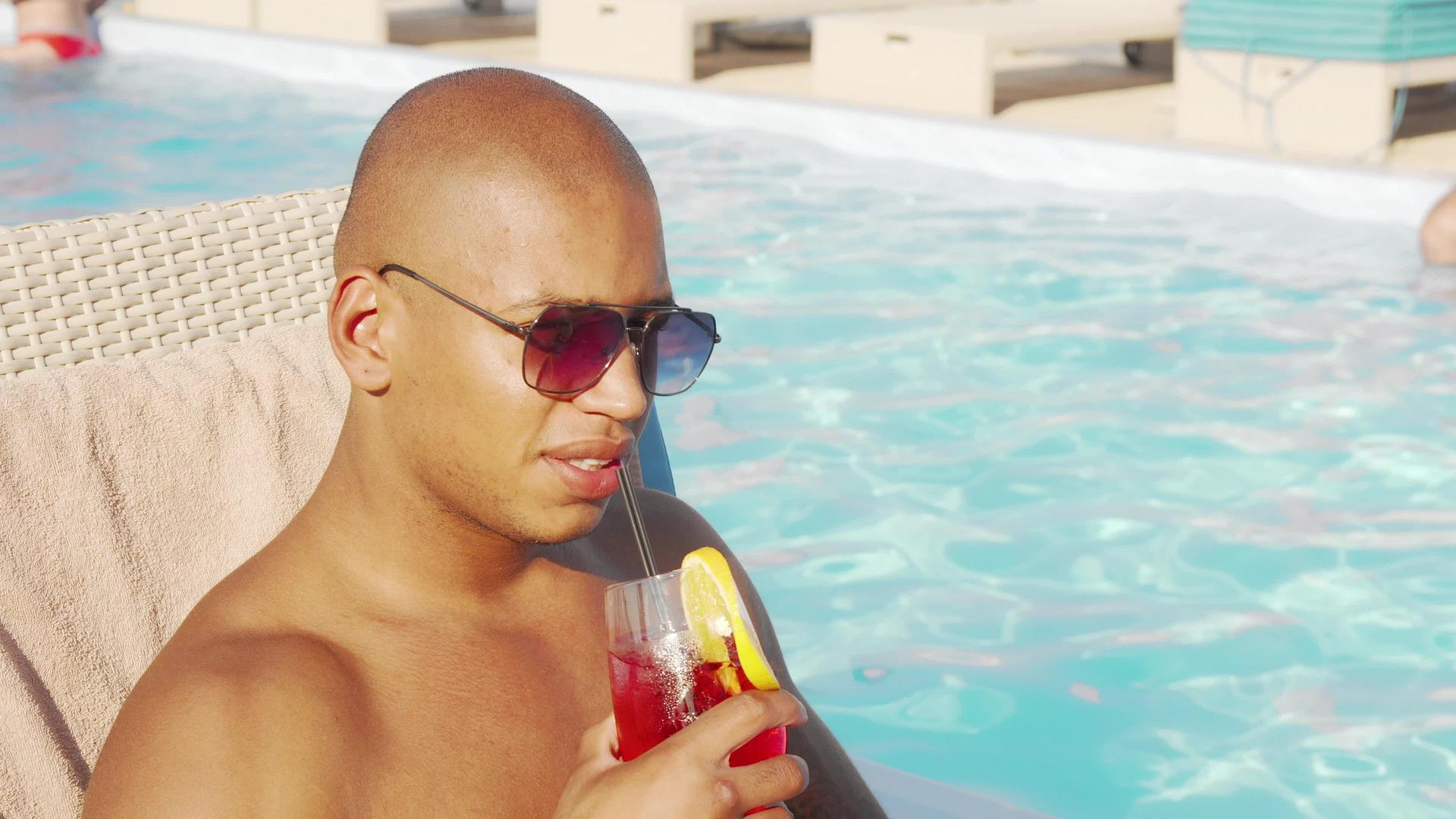 非洲帅帅男在游泳池边喝鸡尾酒坐在游泳池旁边视频的预览图