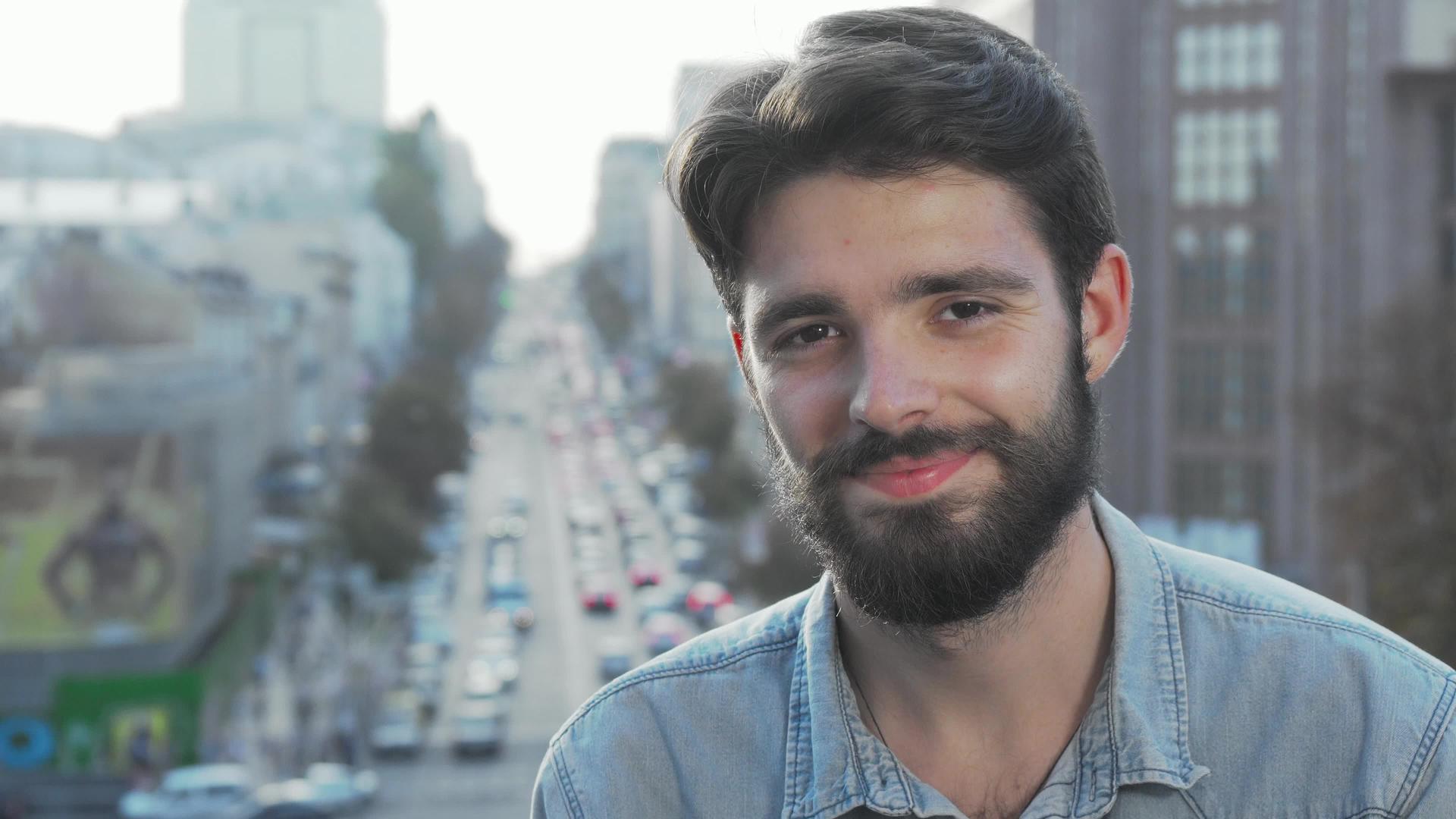 长胡子的年轻人对着相机和城市背景微笑视频的预览图