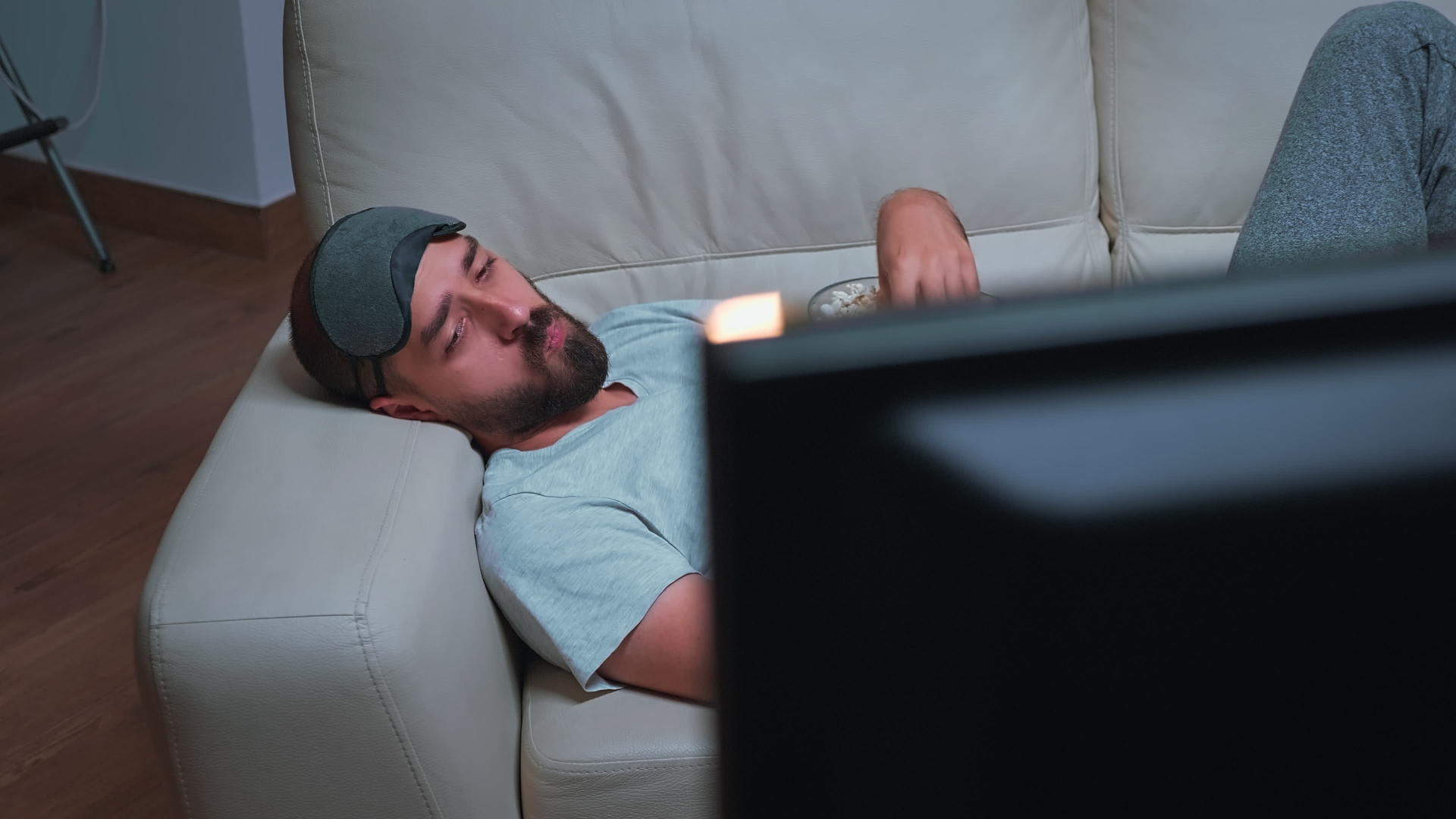 戴眼罩的男人在看娱乐电视节目时吃爆米花视频的预览图