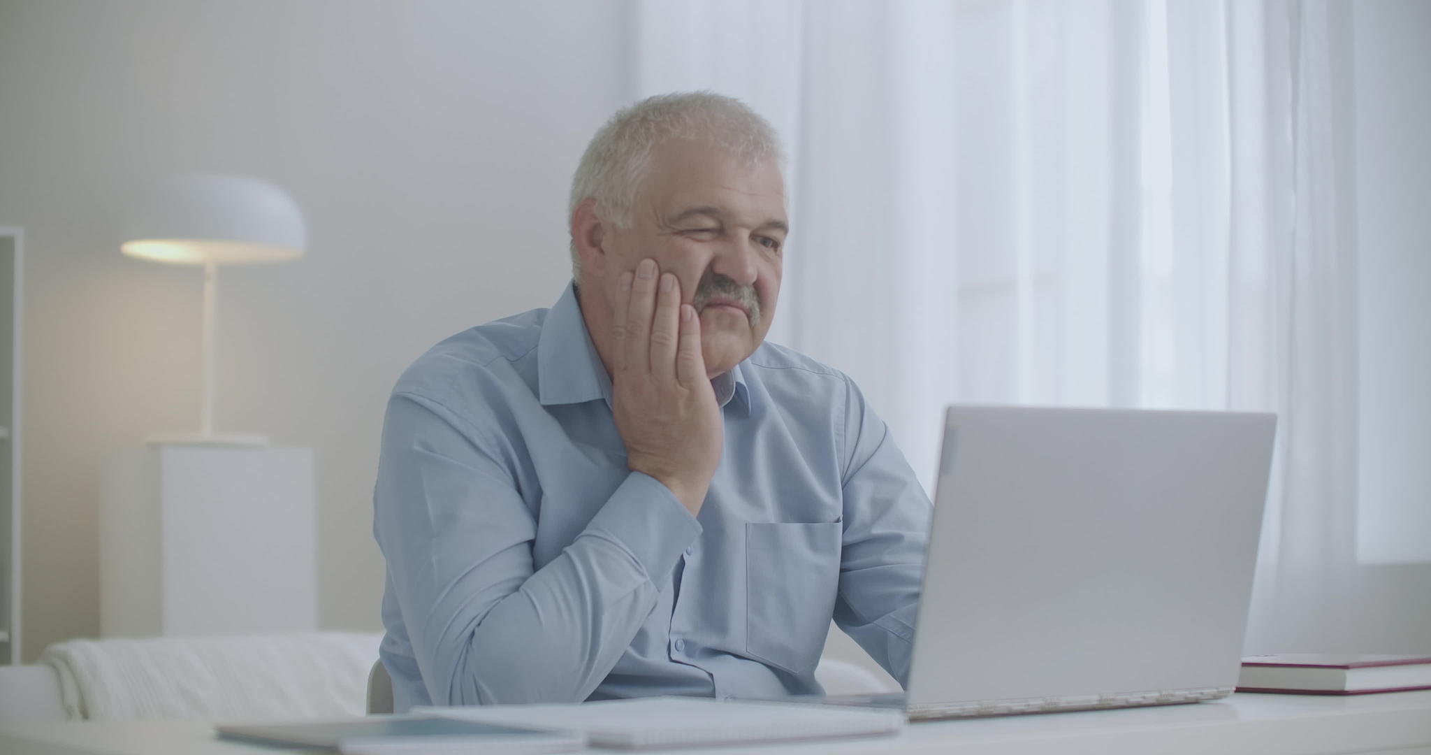 年长的男人在家用笔记本电脑工作感觉尖牙疼工作日摸脸颊视频的预览图