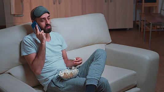 男人在沙发上休息吃爆米花通过电话和朋友聊天视频的预览图