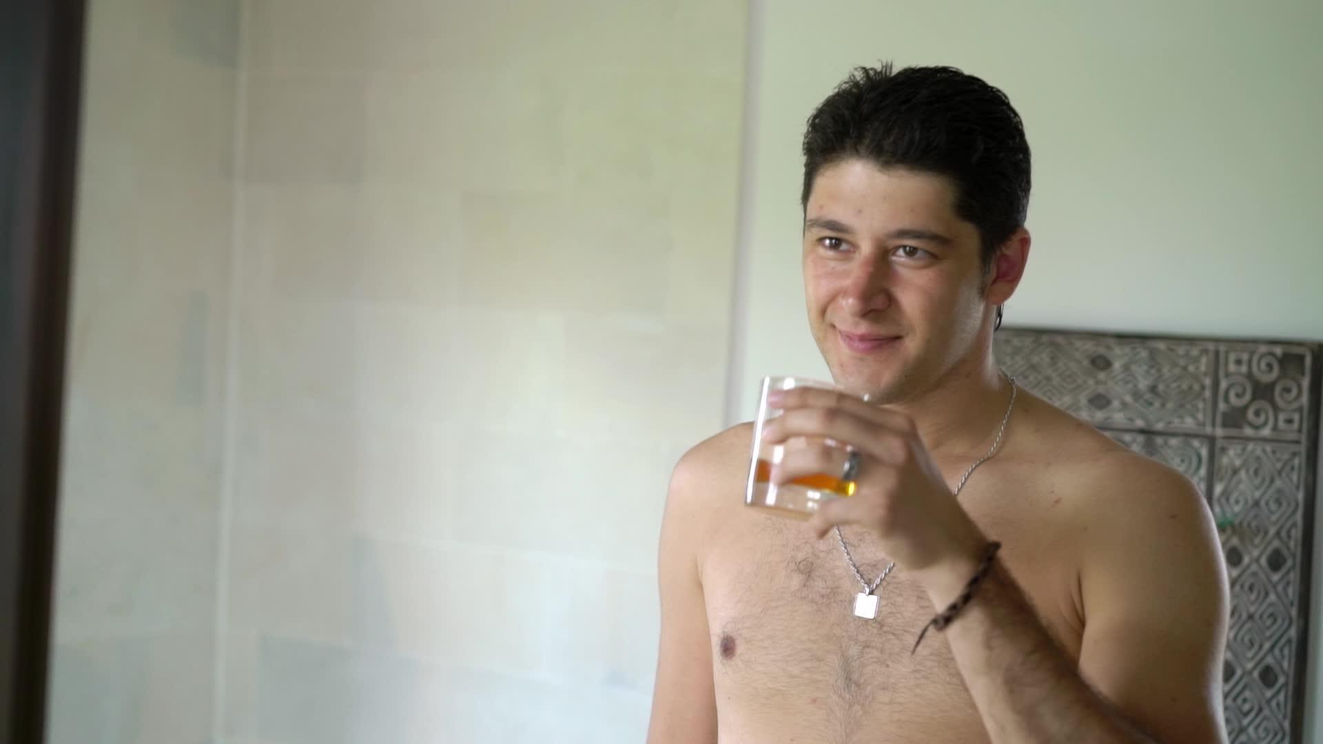 一个没有衬衫、喝威士忌或其他葡萄酒的年轻人在热带别墅度假视频的预览图