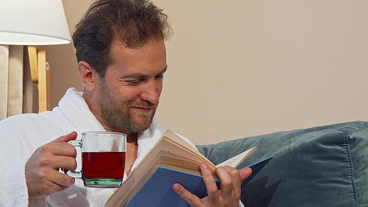 有芳香热茶的成年男子在家看书穿浴袍视频的预览图
