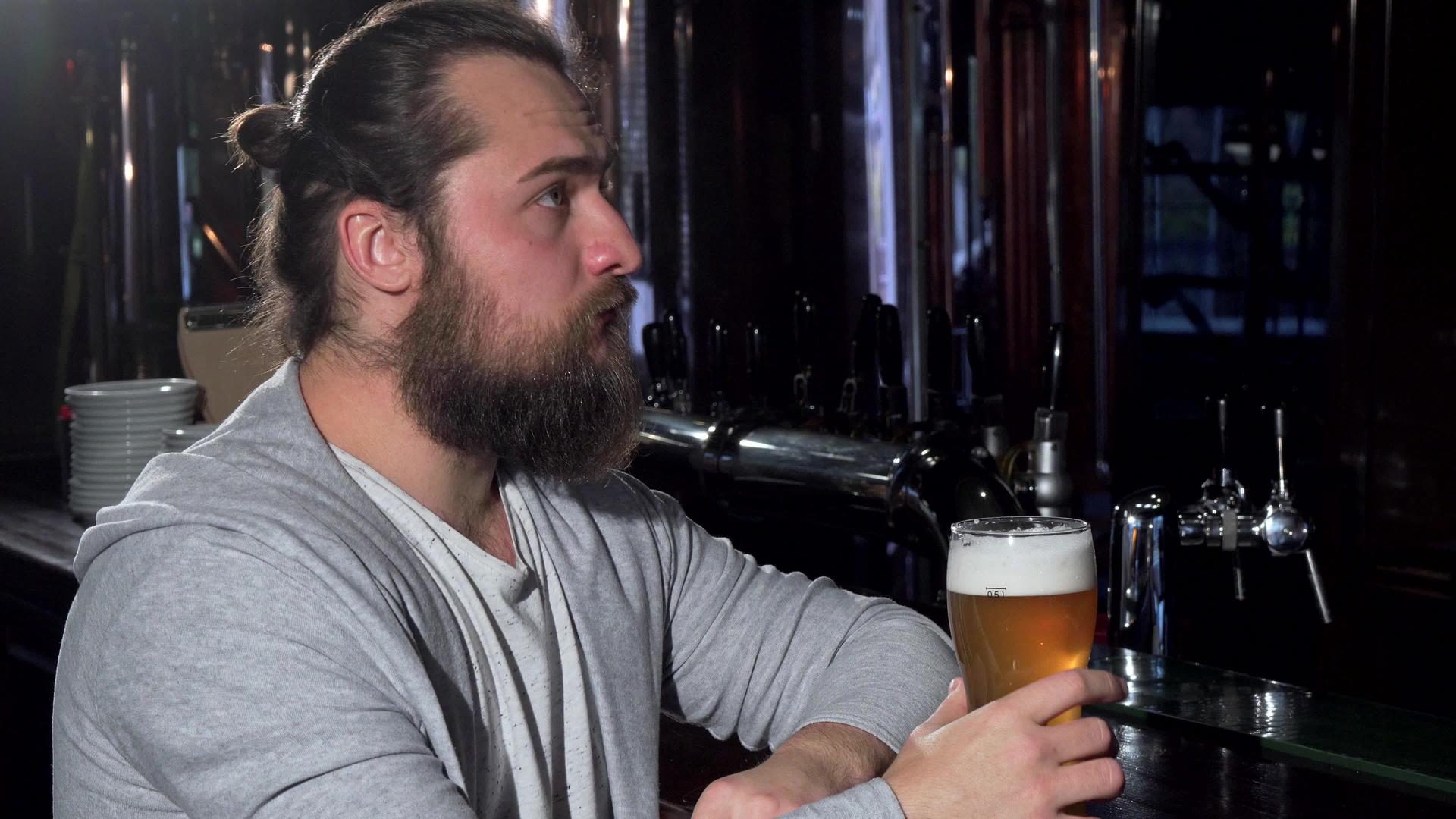 留着长胡子、长发的男人看起来很忧郁独自在酒吧喝啤酒视频的预览图