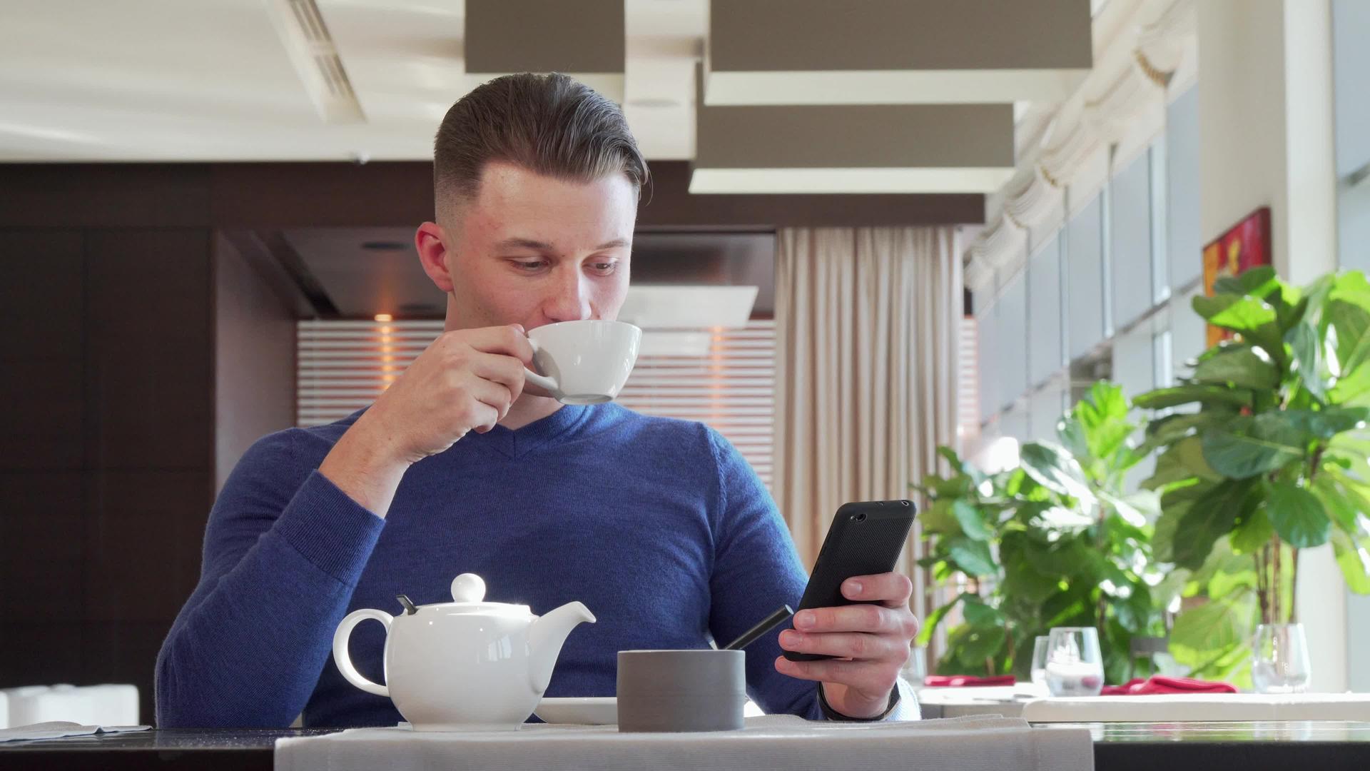 英俊快乐的男人微笑着早餐时在咖啡馆里用他的智慧视频的预览图