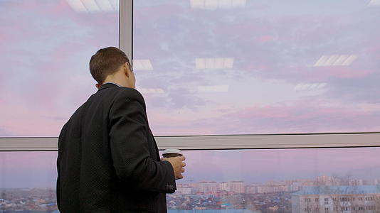 深思熟虑的男人和咖啡透过窗户看着美丽的夜晚天空和城市视频的预览图