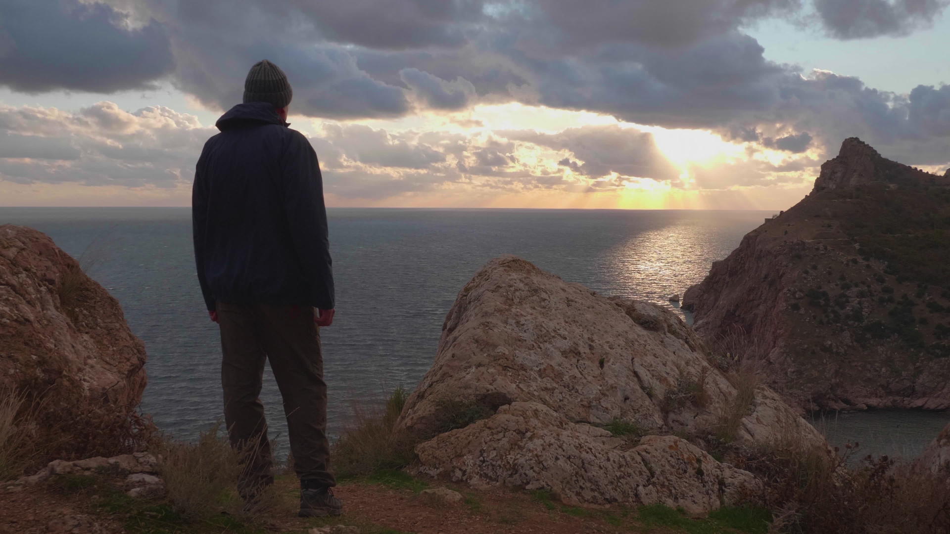 一个穿着夹克和帽子的成熟男人的剪影站在海上岩石悬崖的边缘视频的预览图