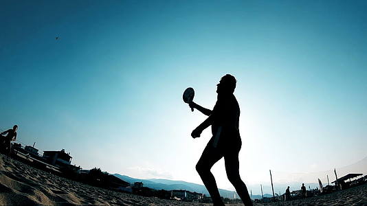 年轻人在岸边玩划桨球在沙滩上慢动作视频的预览图