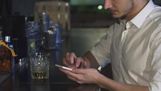 一个人在酒吧喝一杯酒的时候用智能手机把一个男人贴在酒吧里视频的预览图