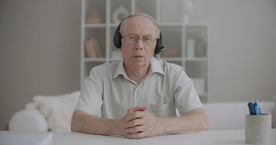 戴着耳机的老人正在观看相机欢迎在线观众并开始学习在线研讨会视频的预览图