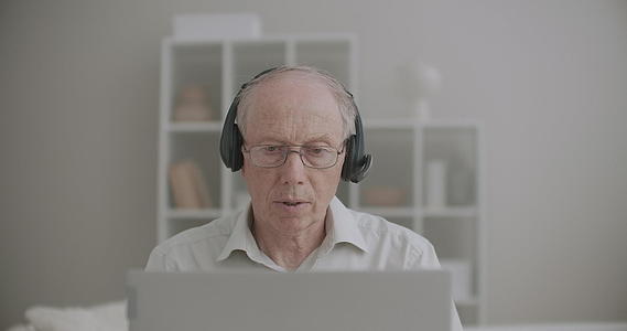 戴耳机的老人正在说话看着笔记本电脑的显示器在家在线讲课视频的预览图