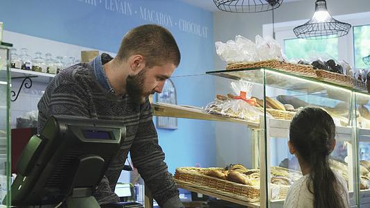 年轻的男面包师在店里工作帮助小女孩选择甜点视频的预览图