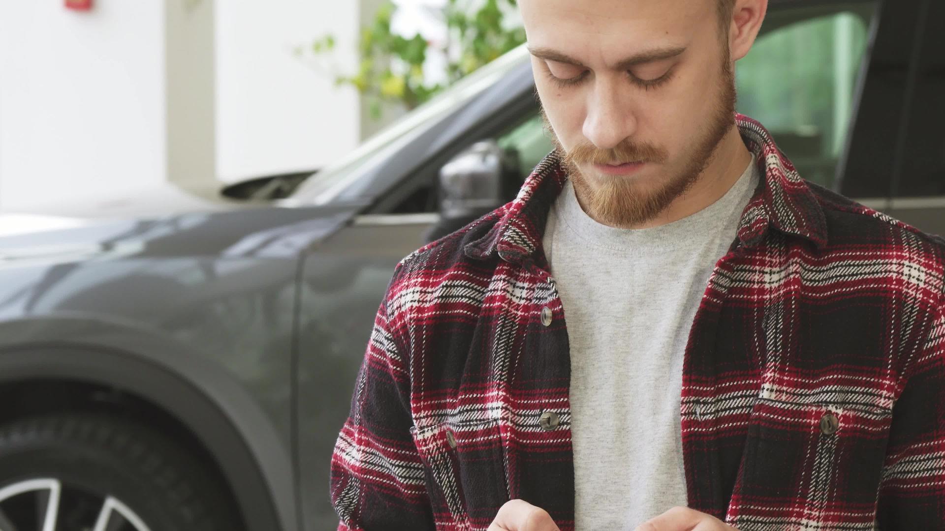 当经销商购买新车时使用智能手机的长胡子英俊的年轻男子视频的预览图