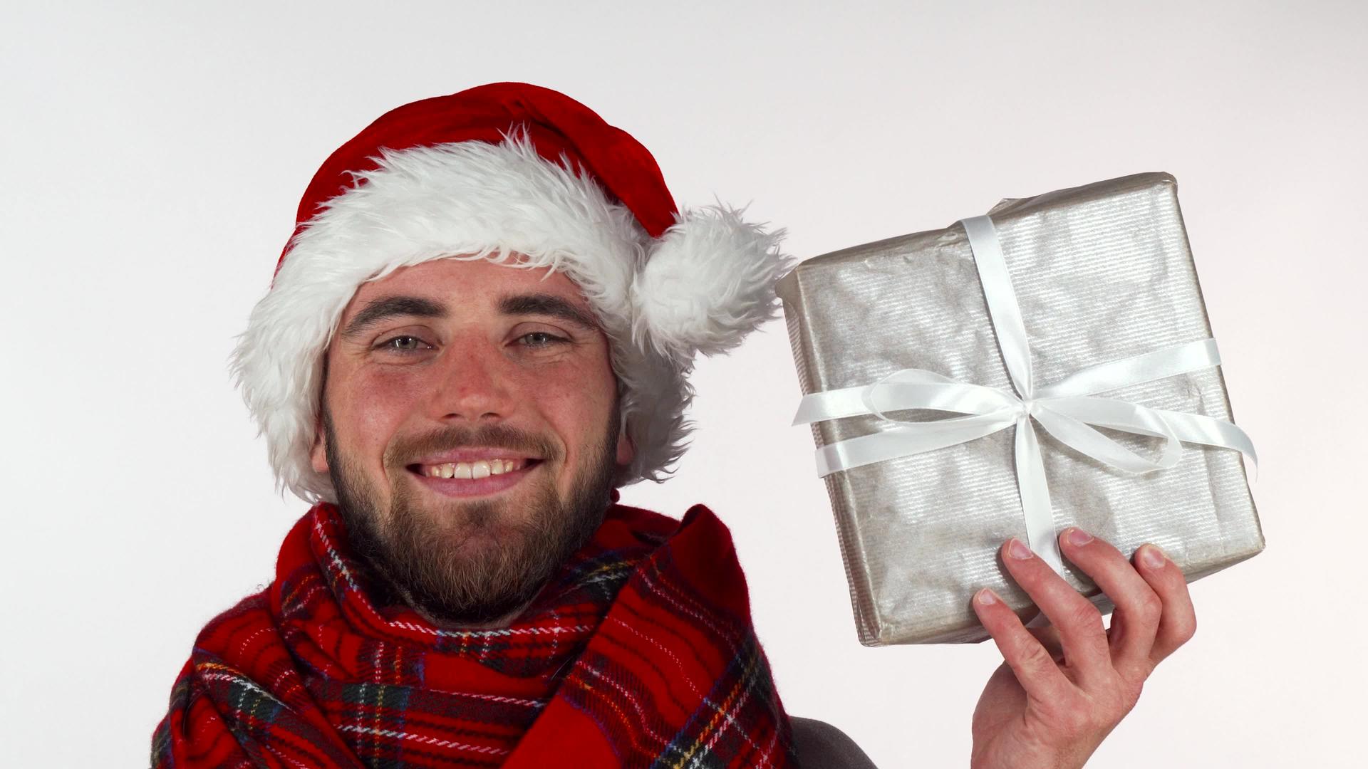 英俊的长胡子男子戴着圣诞帽子微笑着举行礼物视频的预览图