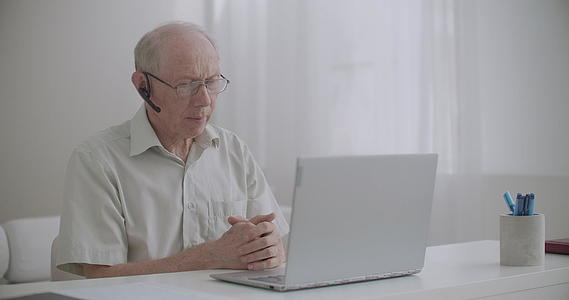 老人坐在家里在笔记本上用视频电话与同事交流视频的预览图