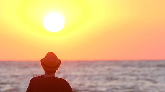 戴帽子的年轻人在海边看日落男性旅行者享受日出和海浪视频的预览图