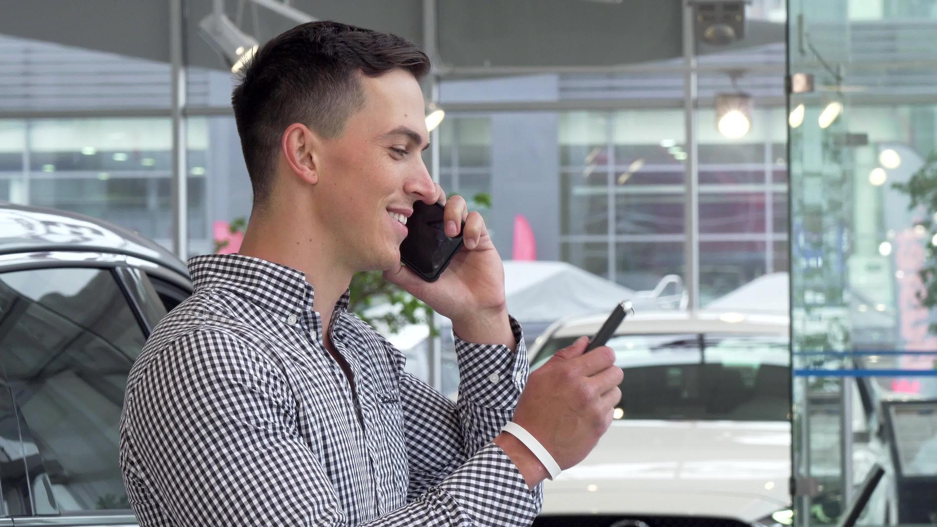男人兴奋的微笑里拿着车钥匙经销商在电话里聊天视频的预览图